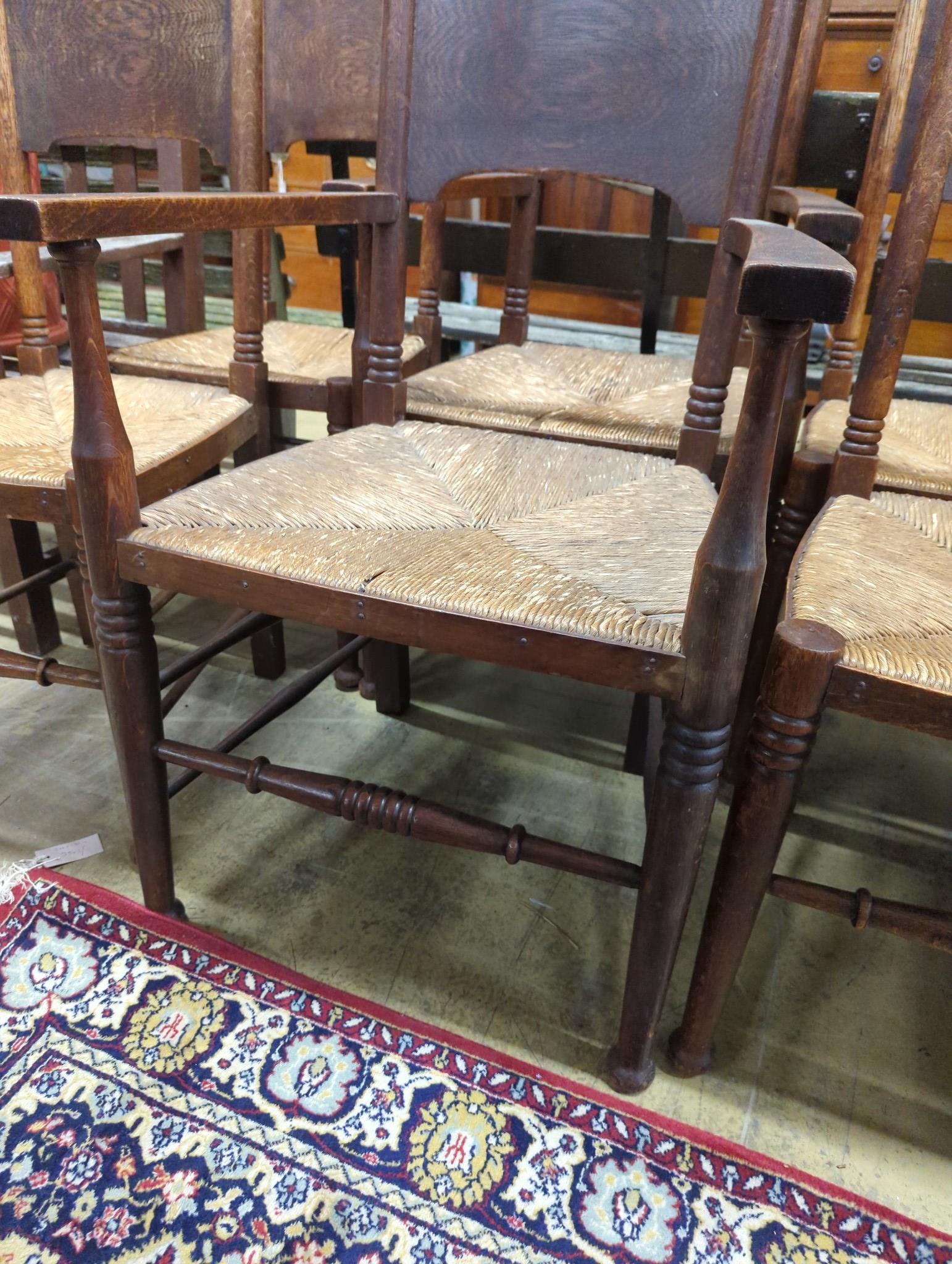 A set of six Arts & Crafts oak chairs, including a pair of carvers, in the Glasgow School manner by William Birch, High Wycombe, with shaped panels backs, ring turned frames and rush seats, carvers W.58cm D.54cm H.109cm